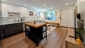 A modern kitchen with a central island, dark cabinets, and a wooden floor. - Bright 2-Bed Ground Suite | Steps to PNE & Transit (Vancouver)