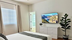 Une chambre à coucher avec un lit, un téléviseur fixé au mur, une plante et une porte donnant sur un balcon.
