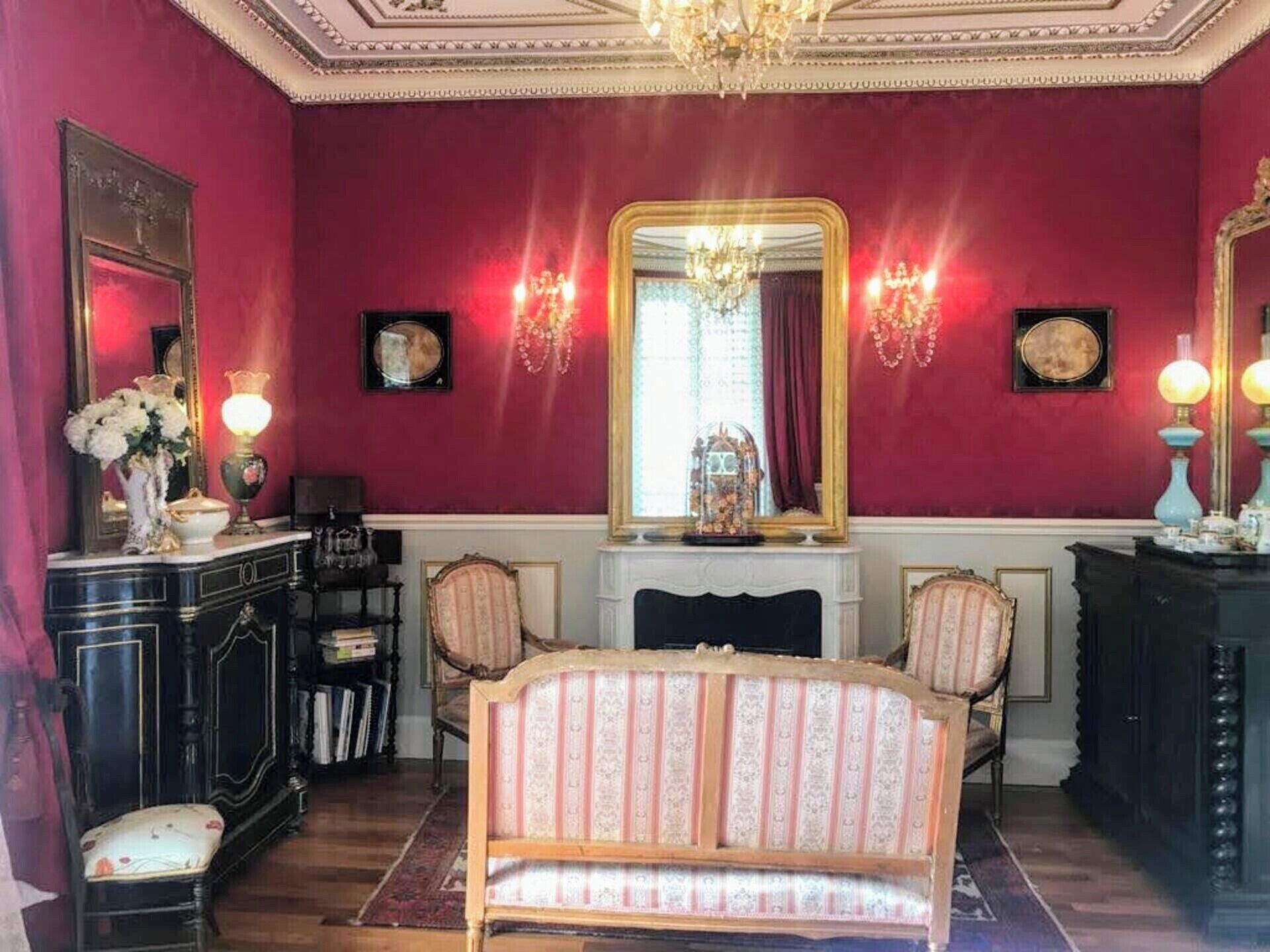 A room with a large mirror, a chandelier, and a bed with striped bedding.