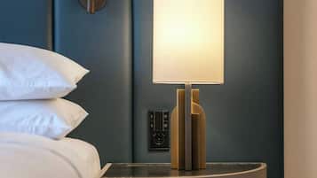 Una camera d'albergo con un letto, un comodino con una lampada e un pannello di controllo a parete.