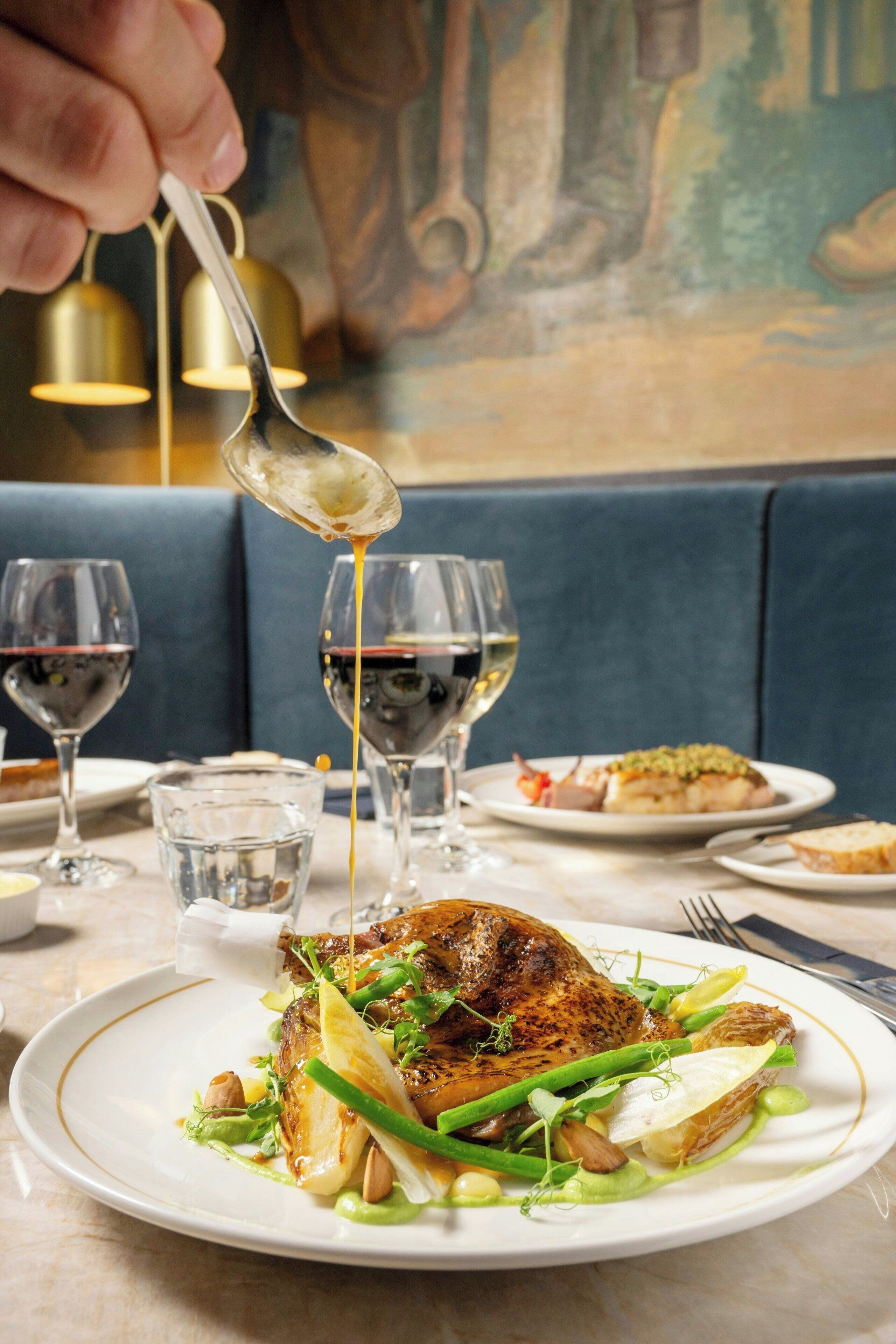 A dining table with a plate of food, wine glasses, and a spoon pouring sauce.