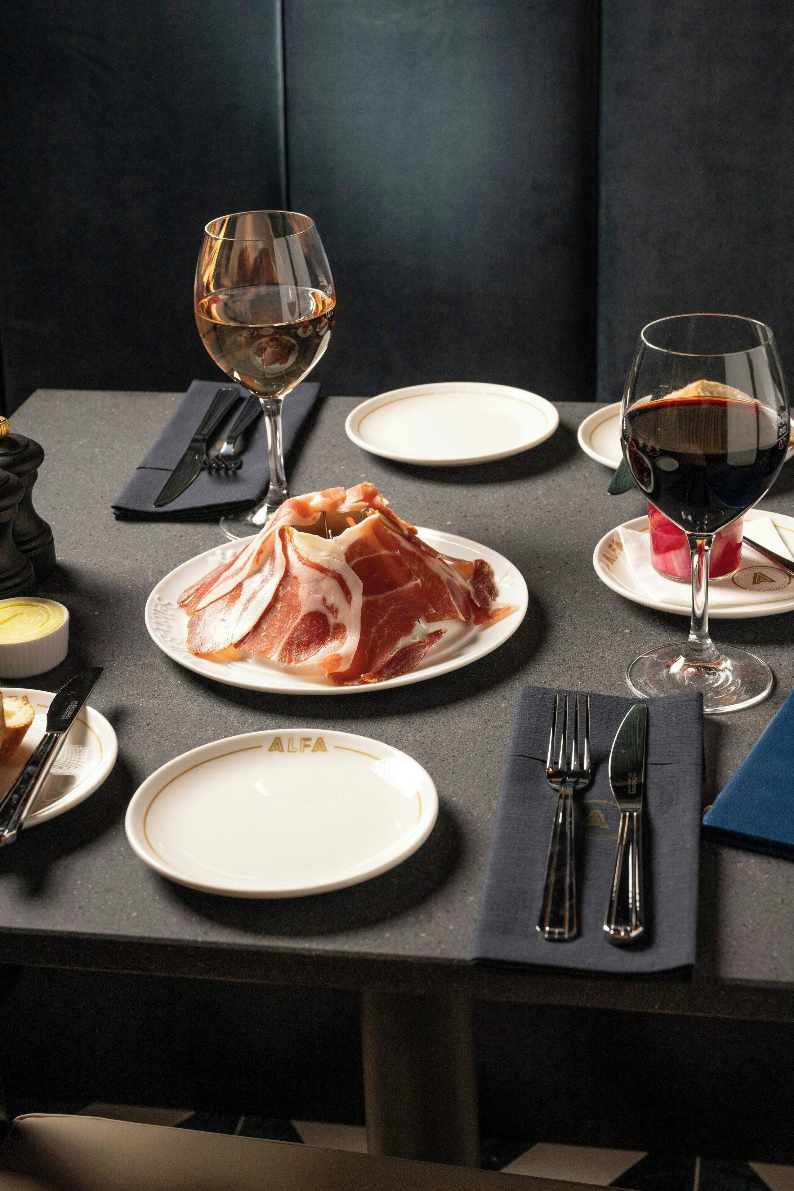 Mesa posta para refeição, com pratos de comida, copos de vinho e talheres.