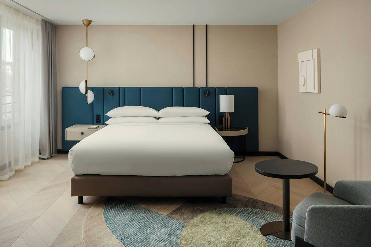 Une chambre d’hôtel moderne avec un grand lit, des tables de chevet, une table ronde et une chaise.