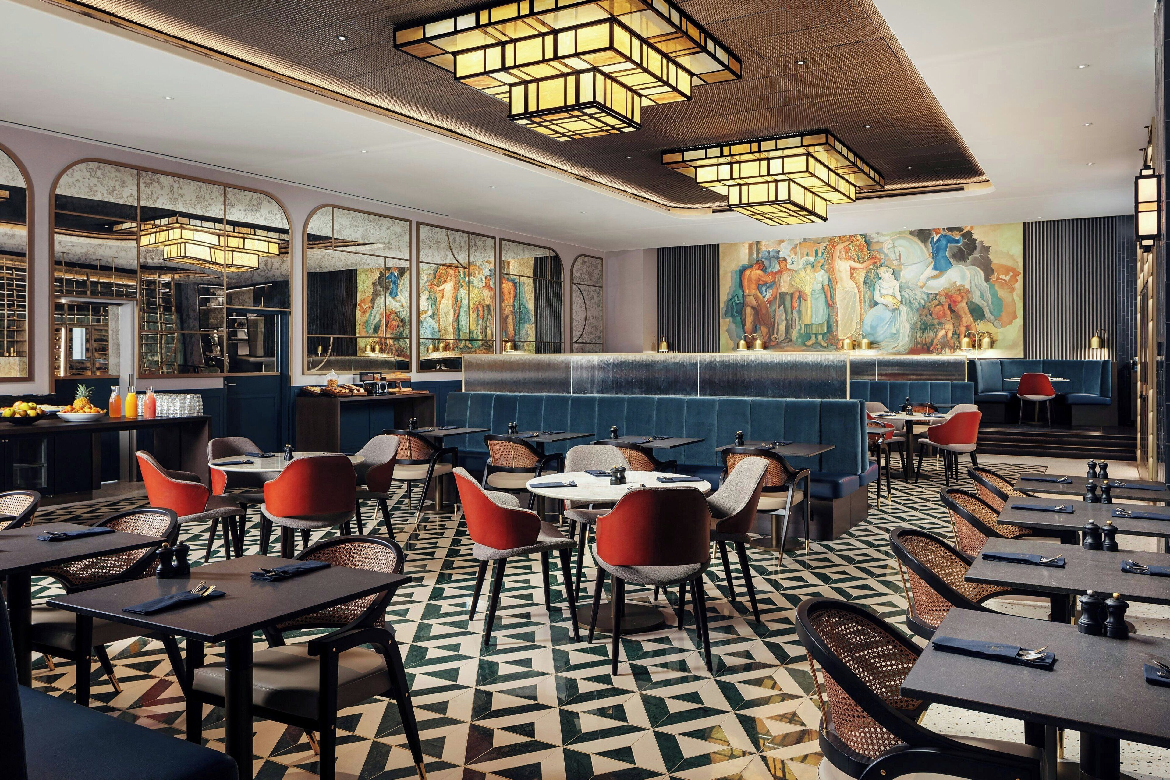 A modern restaurant with a geometric patterned floor, round tables, and red chairs.