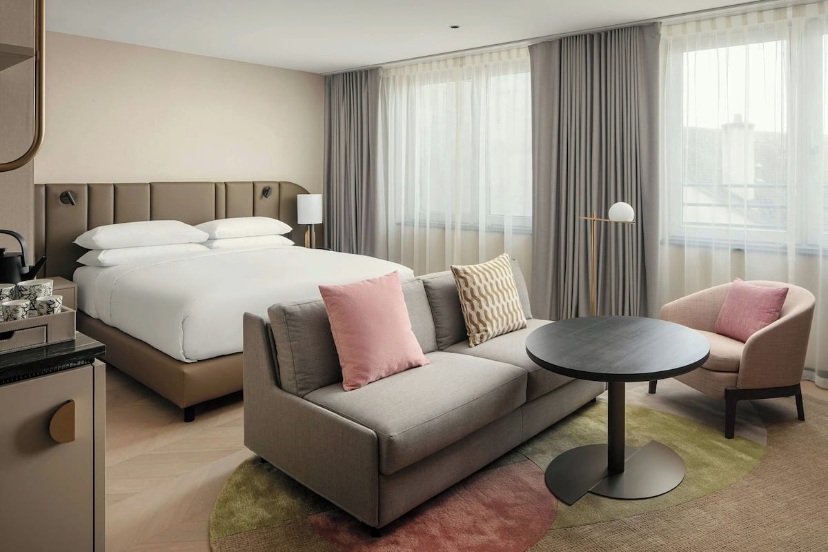 Une chambre d’hôtel moderne, équipée d’un lit, d’un canapé, d’un fauteuil et d’une petite table.
