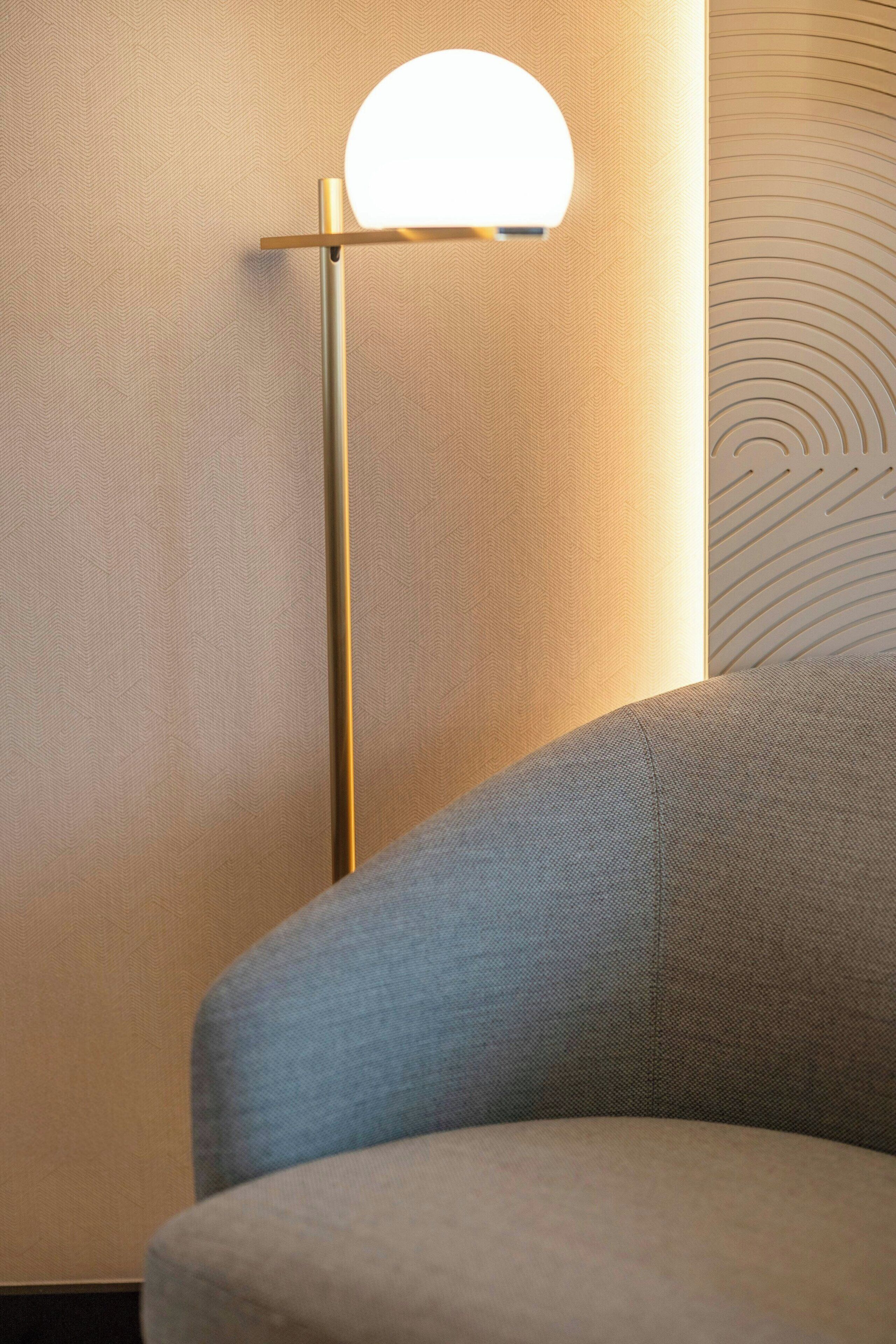 Eine moderne Lampe mit kugelförmigem Lampenschirm, einer strukturierten Wand und einem Teil eines Sofas.