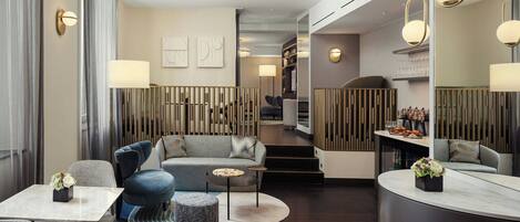 Un moderno vestíbulo de hotel con un sofá, sillas, una mesa redonda y una escalera que sube a otro nivel.