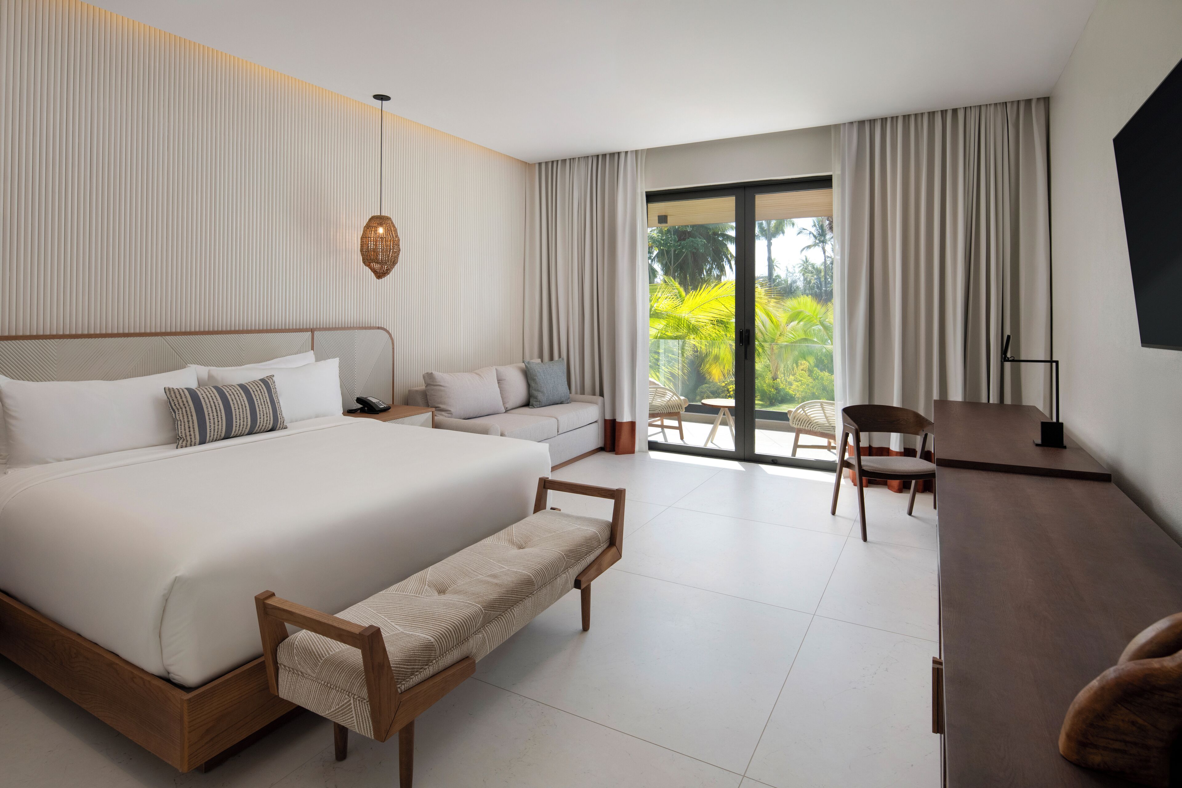 Une chambre d’hôtel moderne, dotée d’un grand lit, d’un canapé, d’un bureau et offrant une vue sur l’extérieur.