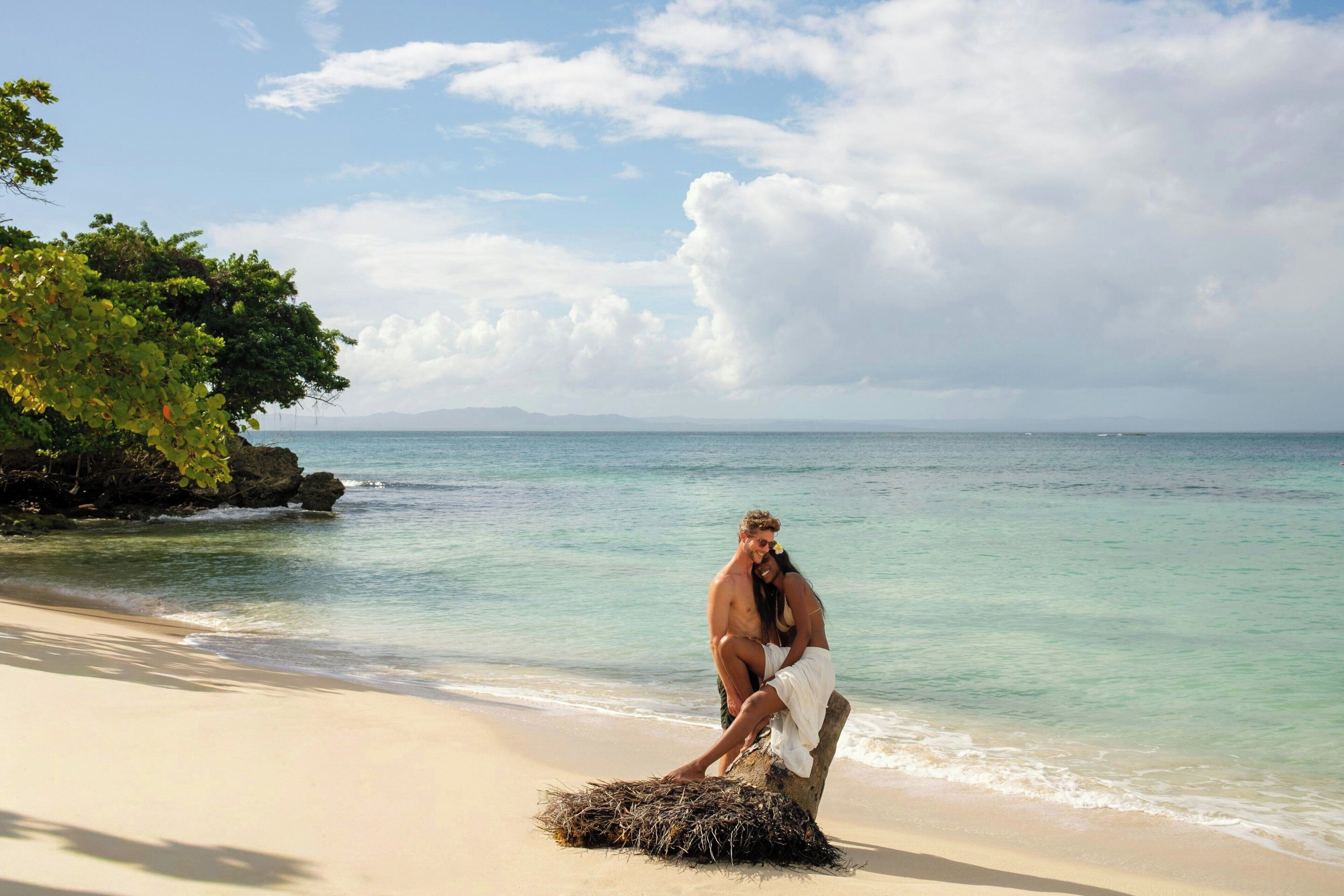 Une scène de plage où un couple est assis sur un rocher, au bord de l’eau.