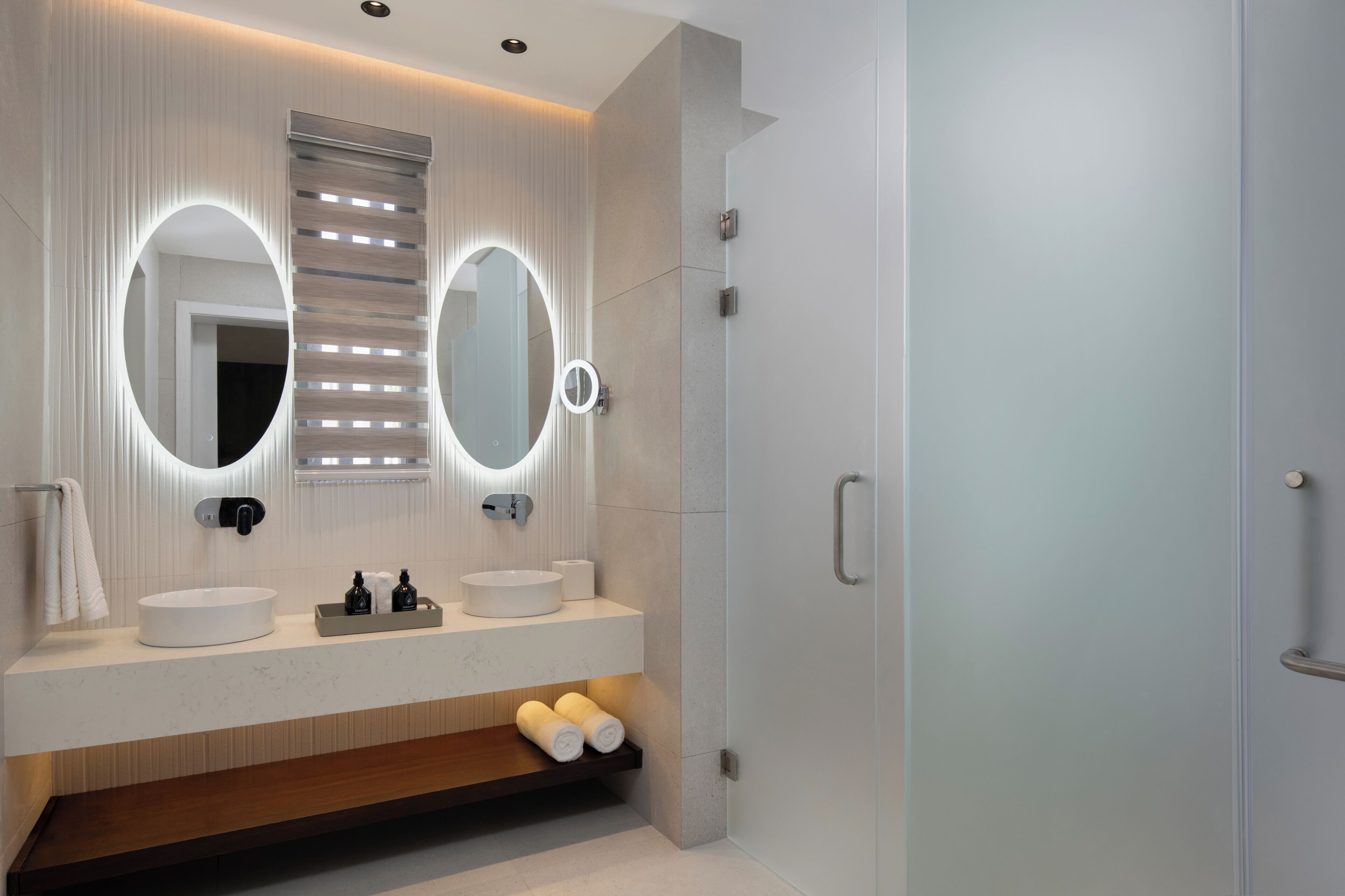 Een moderne badkamer met twee grote spiegels, een rond wastafel en een inbouwkastje met handdoeken.