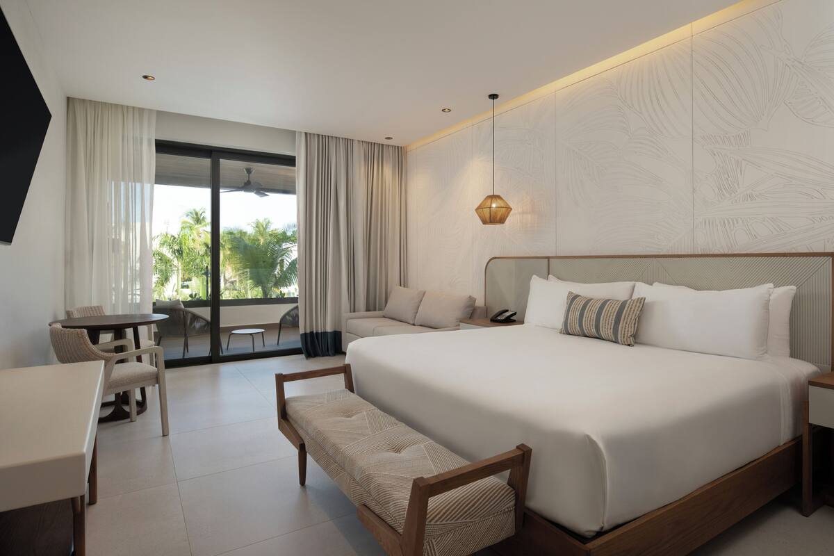 A modern hotel room with a large bed, a small desk, and a bench.