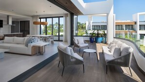 A modern living room with a sofa, chairs, and a coffee table. There is a large window with a view of palm trees and buildings. - Donoma Las Terrenas Resort & Villas Autograph Collection (Las Terrenas)