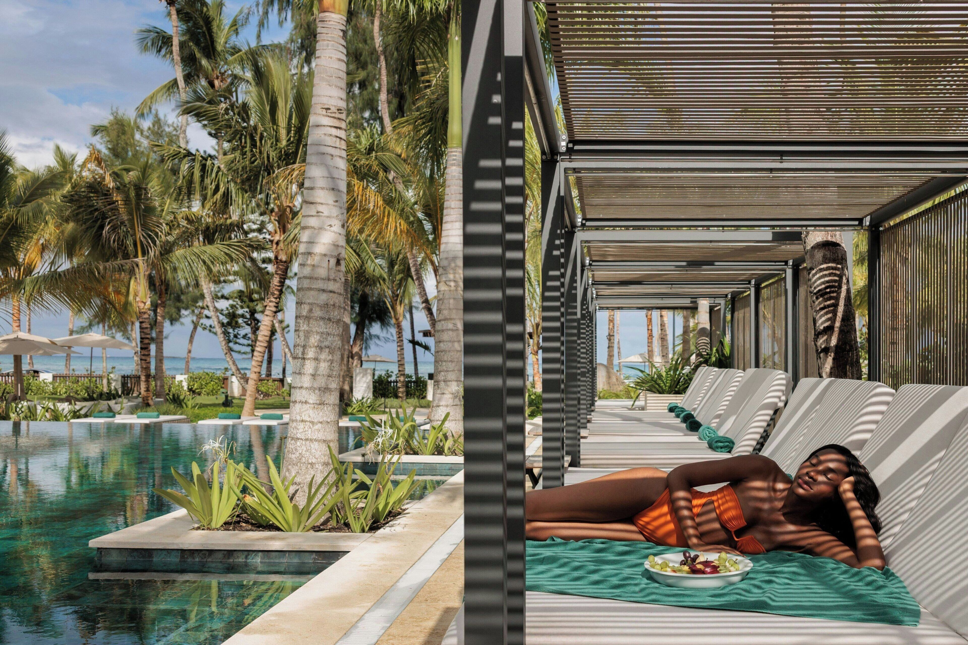 A poolside area with lounge chairs, palm trees, and a clear view of the ocean.