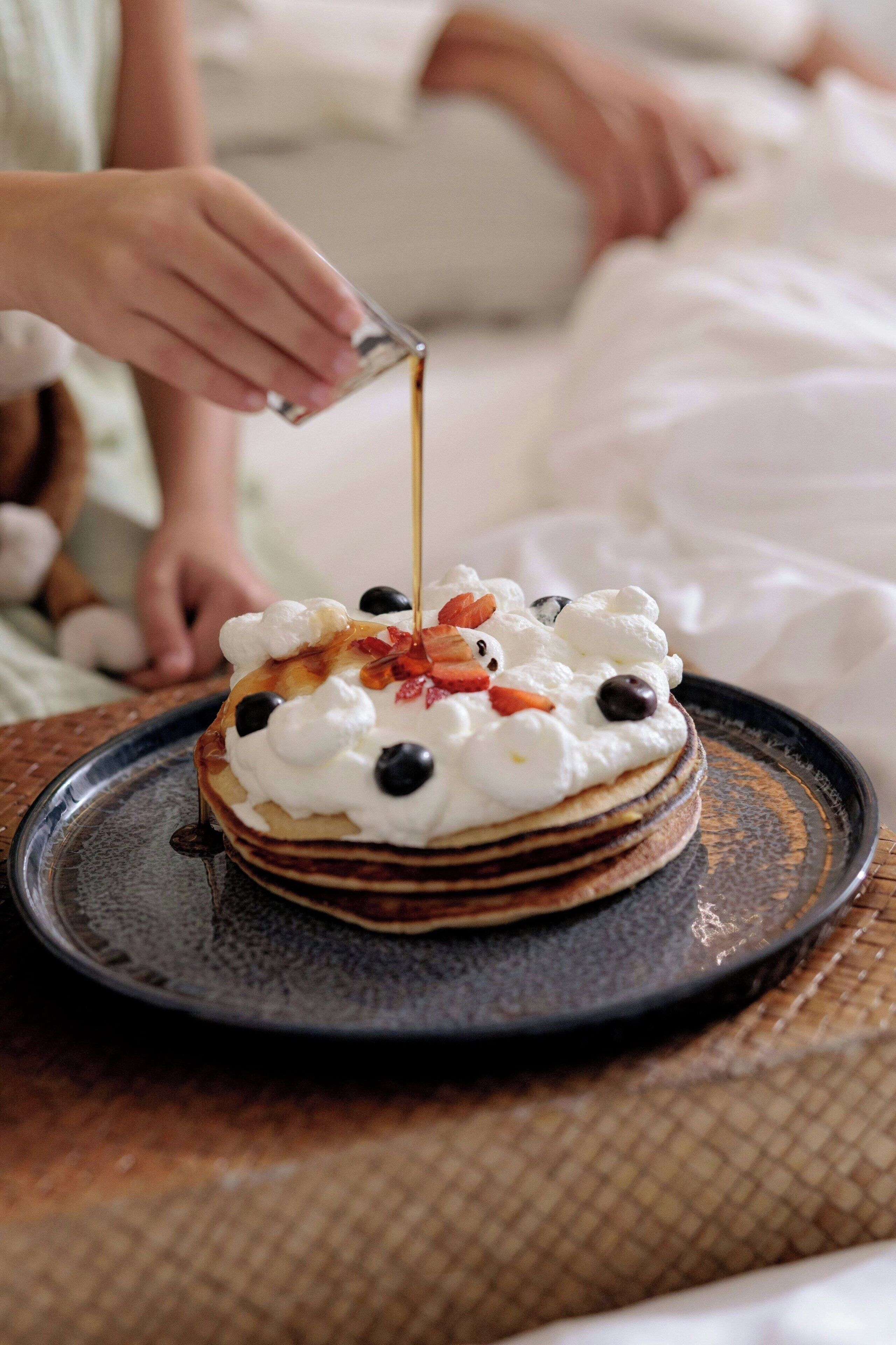 A stack of pancakes with whipped cream and toppings on a plate.