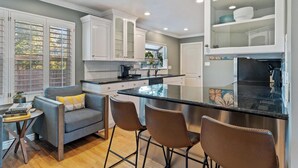 A modern kitchen with white cabinets, a central island, and a dining area with a grey sofa and brown chairs.