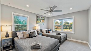 A bedroom with two beds, a ceiling fan, and large windows offering views of the outdoors.