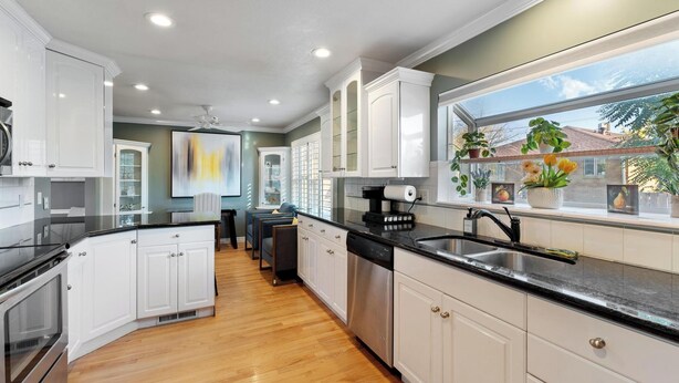 A modern kitchen with white cabinets, a black countertop, and a stainless steel sink. There is a window with plants on the counter.