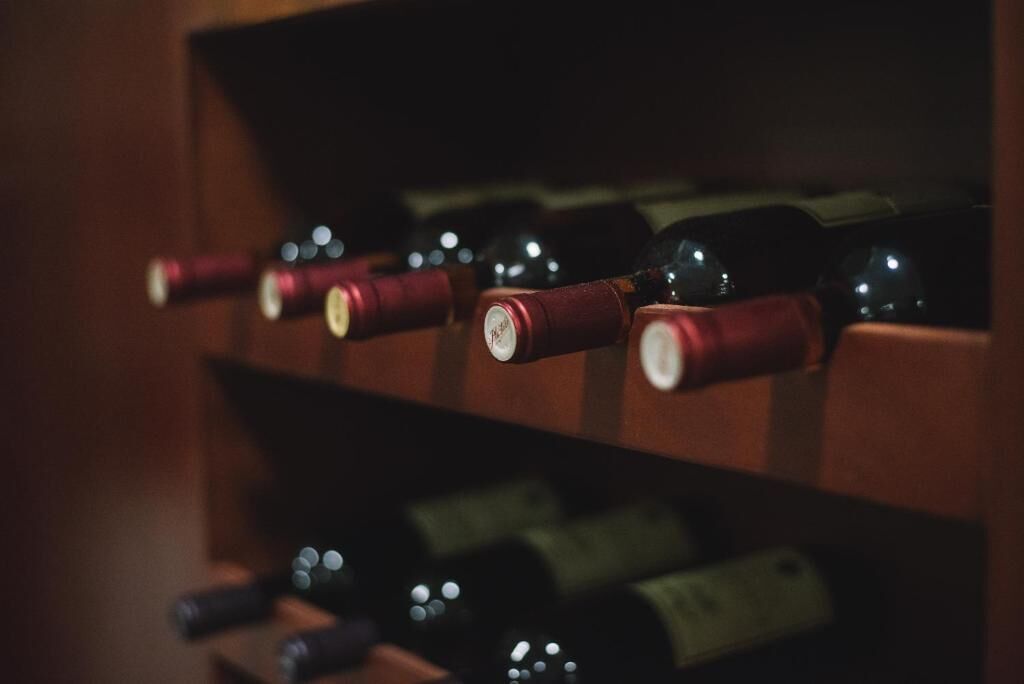 Botellas de vino en fila con corchos en un estante de madera.