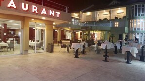 A restaurant with outdoor seating and a two-story building in the background. - Petriti & spa (Ulcinj)