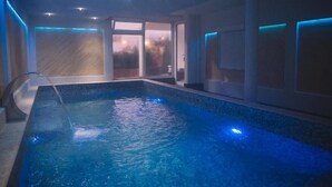 An indoor swimming pool with clear water, a diving board, and a glass door leading outside. - Petriti & spa (Ulcinj)