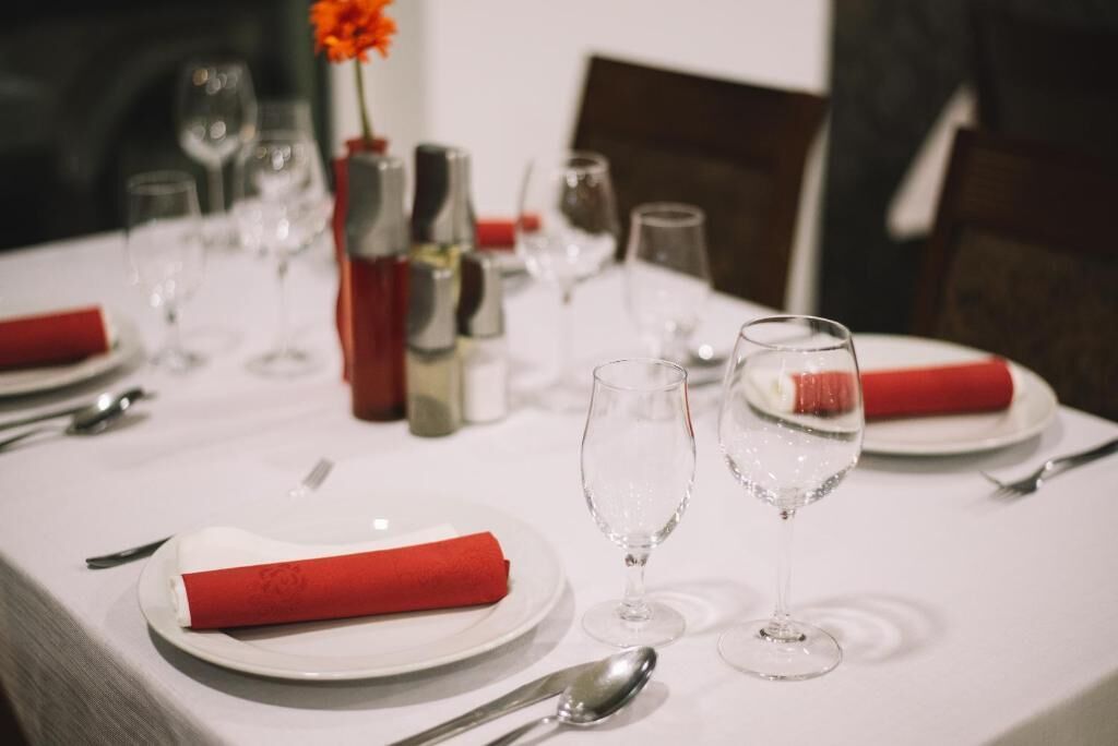 A dining table set with plates, cutlery, and glasses, with a red napkin and a vase with flowers.