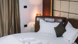 A neatly made bed with white linens and pillows, a brown leather headboard, and a bedside lamp. - Petriti & spa (Ulcinj)