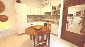 A kitchen with white cabinets, a wooden dining table, and a large mirror. - Pisu Apartments (Bonarina apartment)  (Quartucciu)
