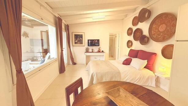 A cozy bedroom with a bed, a bedside table, and a window with curtains. - Pisu Apartments (Bonarina apartment)  (Quartucciu)