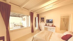 A bedroom with a bed, a desk, a TV, and a shower. - Pisu Apartments (Bonarina apartment)  (Quartucciu)