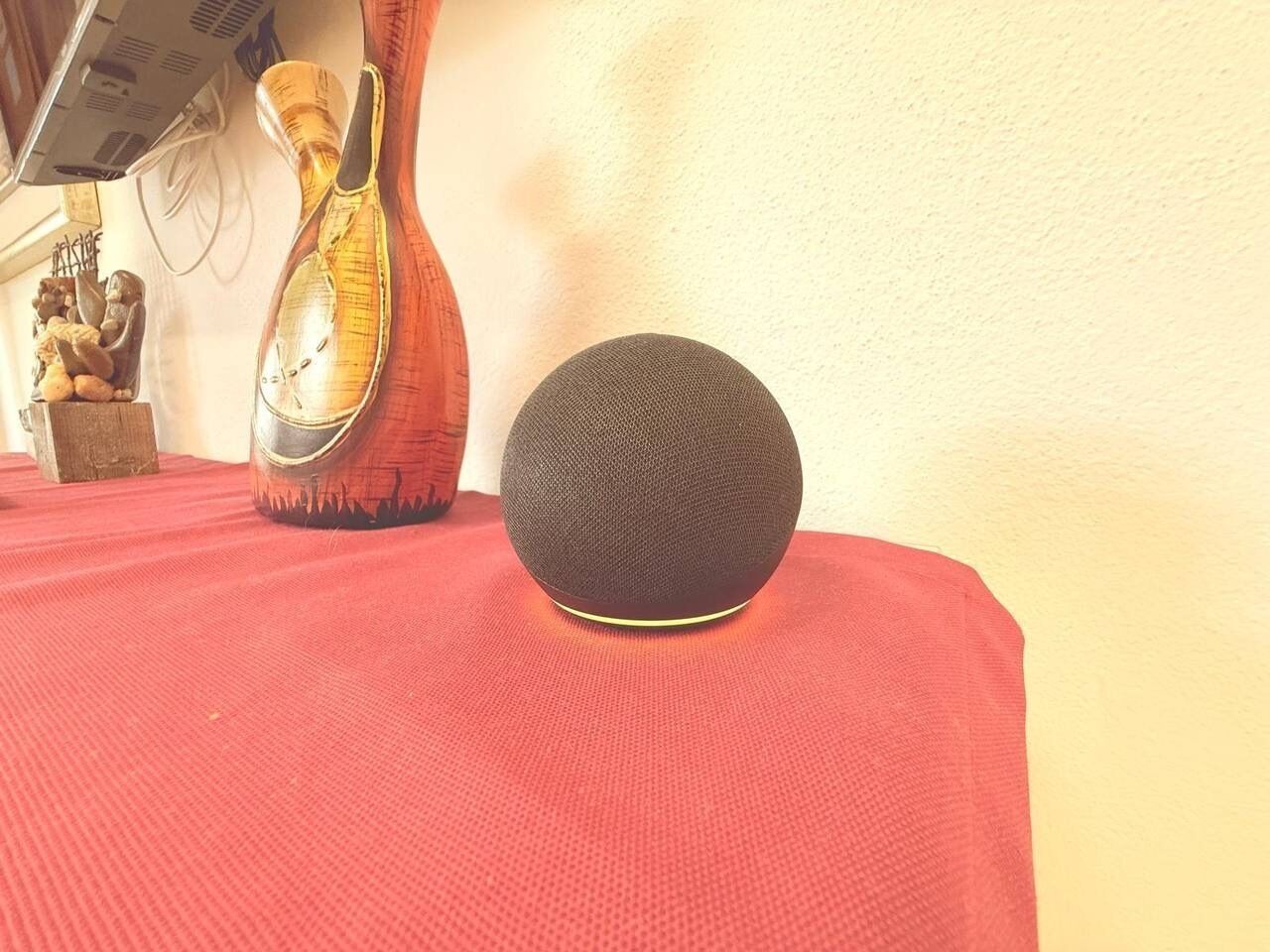 Ein rundes, strukturiertes Objekt auf roter Oberfläche, im Hintergrund eine Vase und eine Statue.