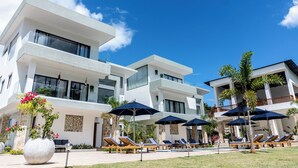 A modern hotel with multiple floors, outdoor seating areas with umbrellas, and a pool. - Luxury Villa for 10 Guests with Pool and Jacuzzi (Las Terrenas)