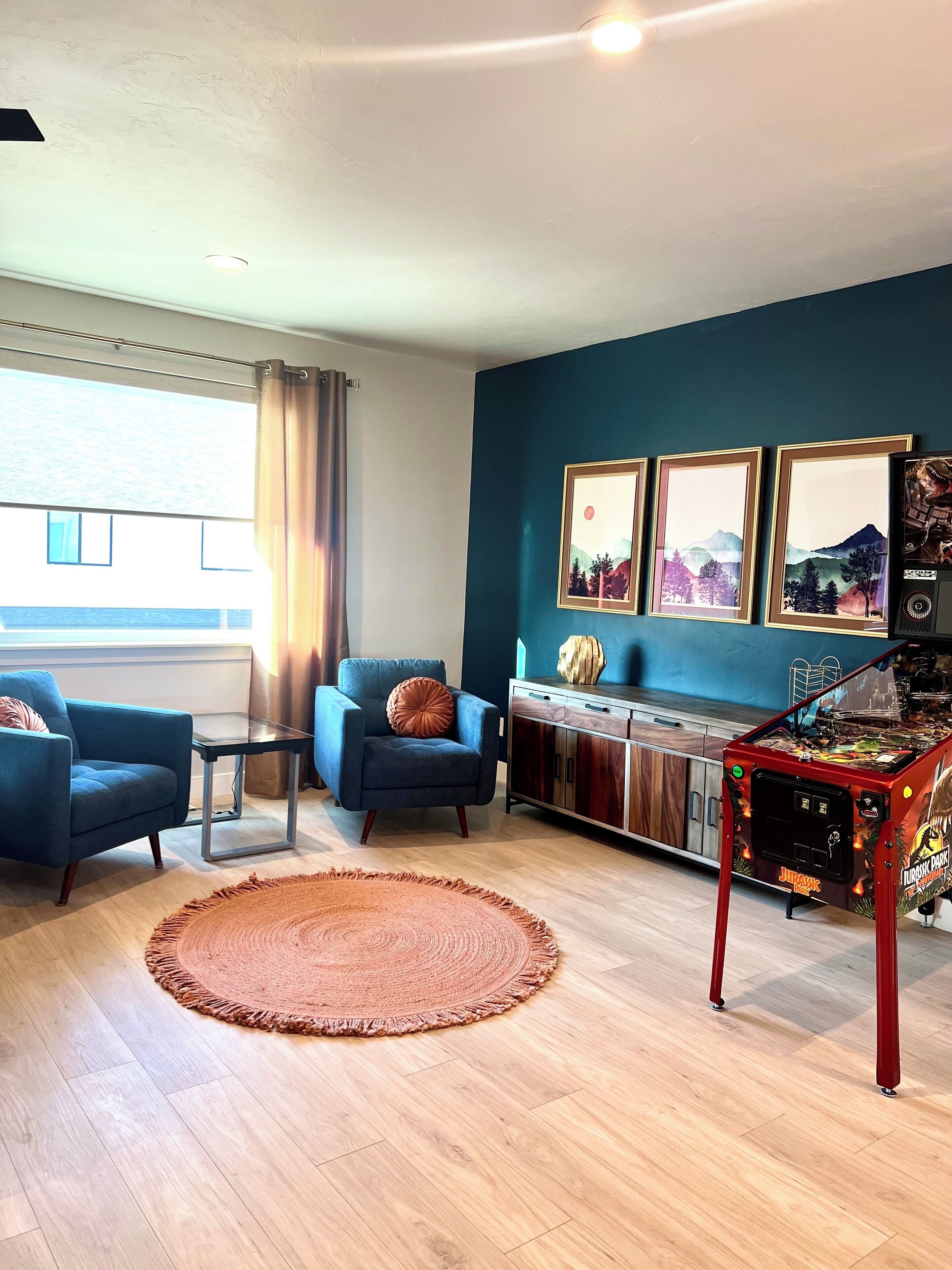 A modern living room with a blue sofa, a coffee table, a rug, and a pinball machine.