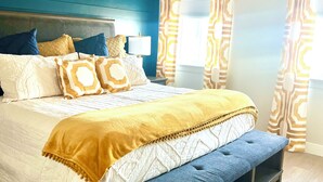 A bedroom with a bed, a bench, a ceiling fan, and patterned curtains.