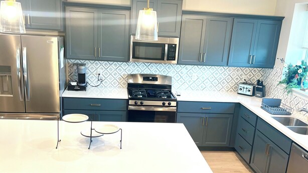 A modern kitchen with grey cabinets, stainless steel appliances, a white island, and striped bar stools.