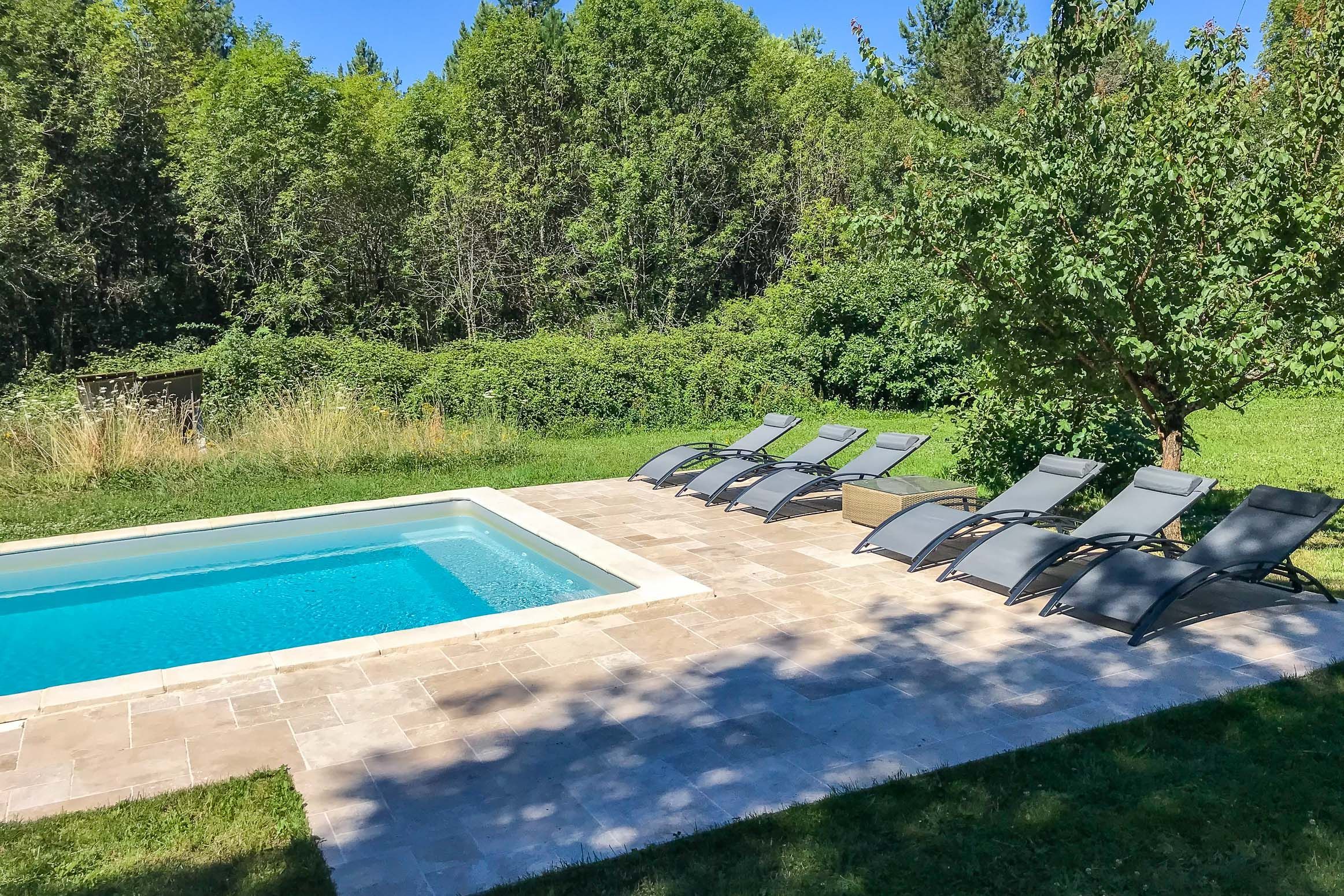 Une piscine entourée d’une terrasse carrelée et de chaises longues disposées tout autour.