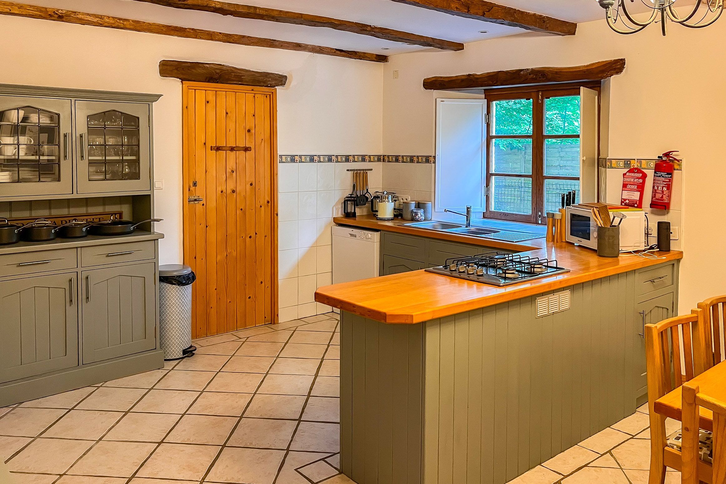 Een keuken met een centraal eiland, houten kastjes, een raam en een brandblusser.