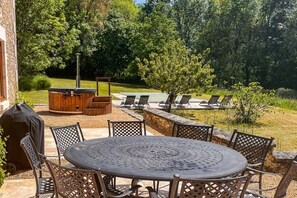 An outdoor patio with a round table and chairs, a barbecue grill, and a hot tub surrounded by lounge chairs. - La Grange Des Epinettes (Teyjat)