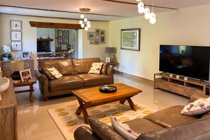 Ein Wohnzimmer mit braunem Ledersofa, einem Holztisch, einem Fernseher und einem Essbereich im Hintergrund.
