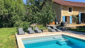 Une piscine avec des chaises longues et, en arrière-plan, un bâtiment en pierre.