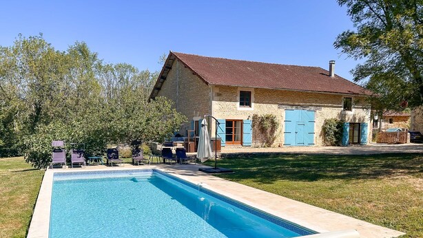 Une maison avec une piscine, du mobilier d’extérieur et une façade en pierre.