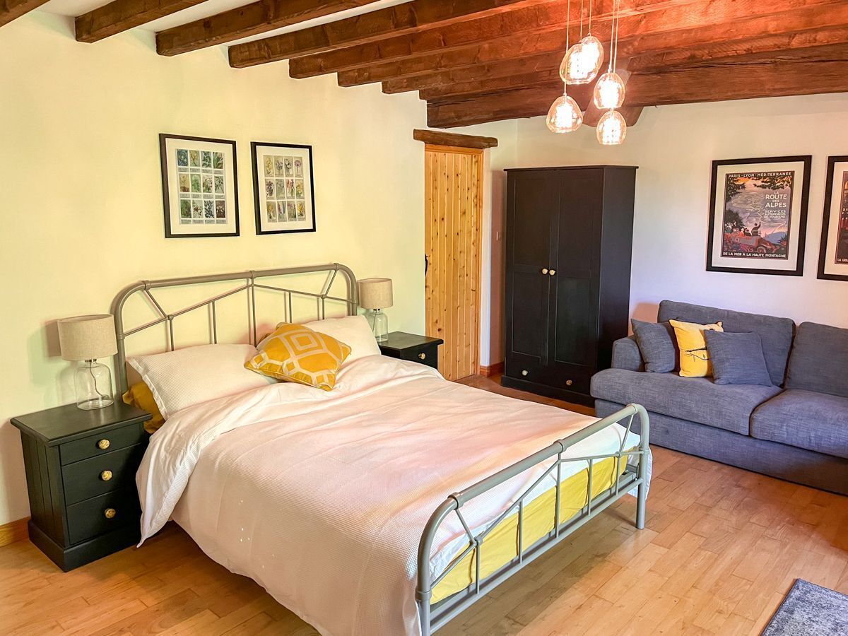 Een slaapkamer met een metalen bedframe, een grijze bank, houten vloeren en een houten plafond.
