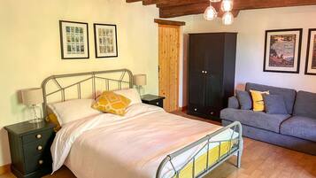 Een slaapkamer met een metalen bedframe, een grijze bank, houten vloeren en een houten plafond.