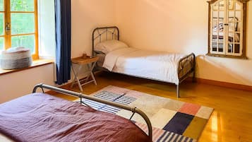 Een kamer met twee bedden, een raam met gordijnen, een houten vloer en een spiegel aan de muur.