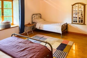 Ein Zimmer mit zwei Betten, einem Vorhangfenster, einem Holzboden und einem Spiegel an der Wand.