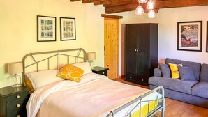 Une chambre à coucher avec un lit en métal, une armoire en bois, un canapé gris et deux reproductions botaniques encadrées accrochées au mur.