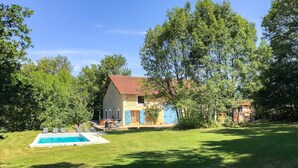 Une maison en pierre à deux étages, dotée d’une piscine, et entourée d’une végétation luxuriante et d’arbres.