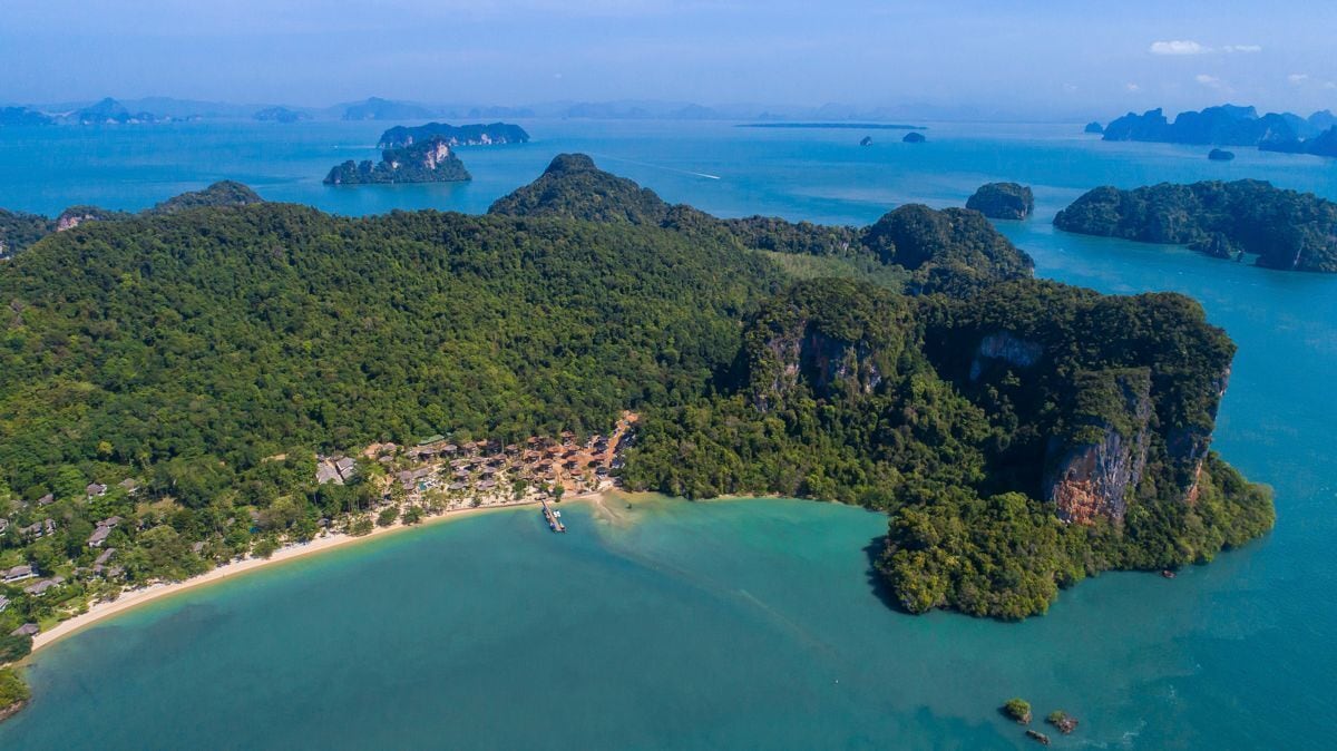 An aerial view of a coastal area with a beach, dense forest, and scattered islands.