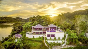 A two-story house with a balcony, surrounded by lush greenery and a lake. - TreeHouse Villas - Hilltop Pool Villa (Ko Yao Noi)