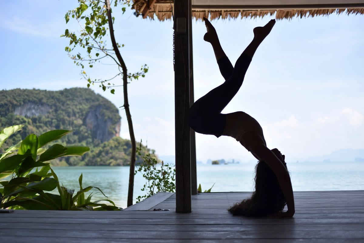A person performing a yoga pose on a wooden deck with a view of a mountainous coastline.