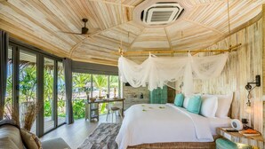 Une chambre spacieuse avec un grand lit, un coin salon avec une table et des chaises, et une vue sur la verdure grâce à de grandes fenêtres.